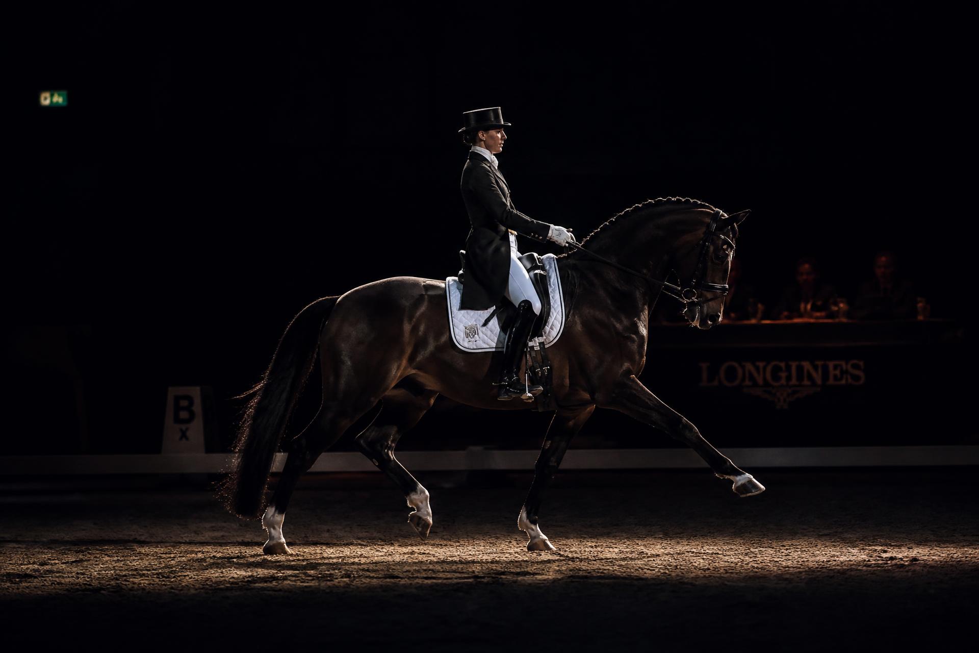 Dressage rider in extended trot in a dim arena
